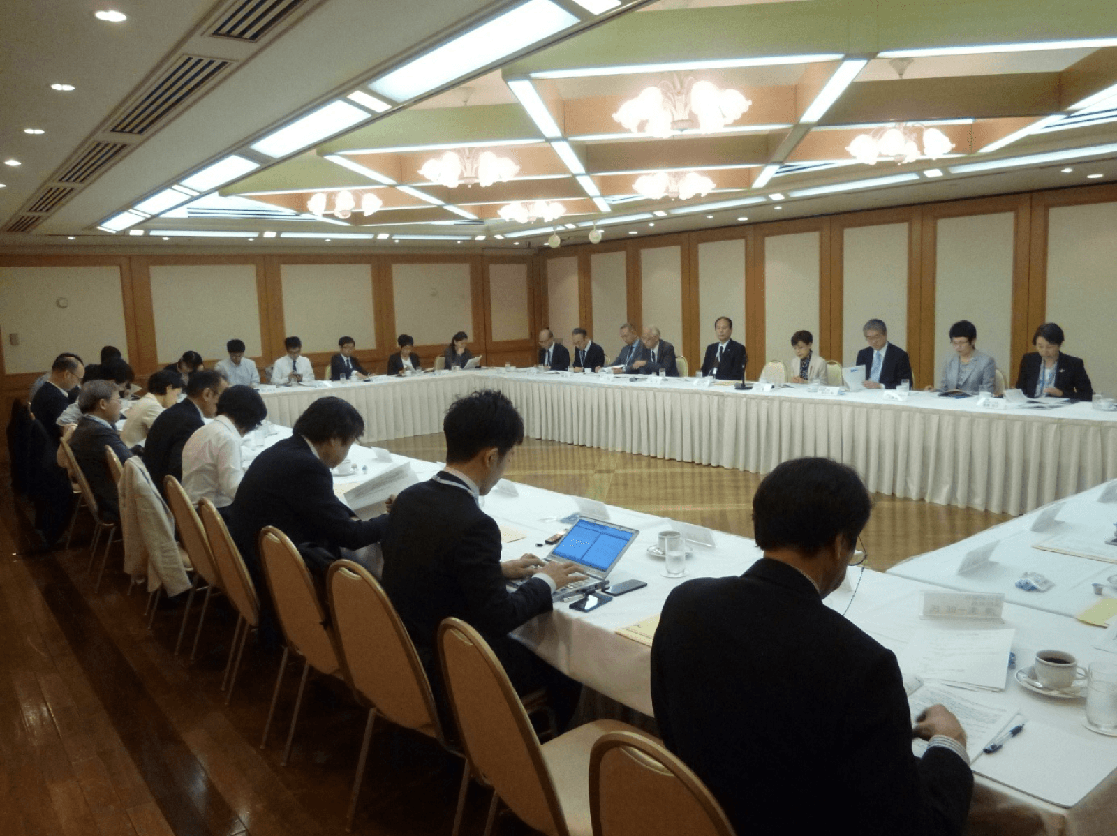 記者懇談会の会場で、多くの報道関係者を前に登壇者が説明している様子。