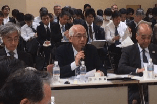 文部科学省の会議室で、委員が着席して意見を述べている様子。